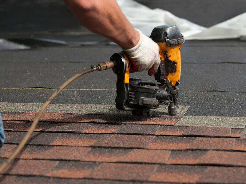 Roof installer nailing down shingles with nail gun