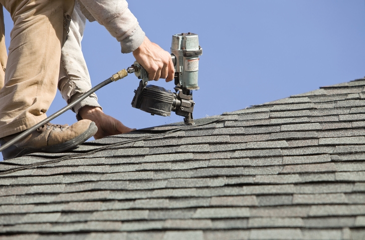 Roof worker using nail gun to install roof shingles